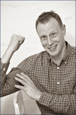Geschäftsinhaber Peter Wieske ballt eine Faust und hebt den Arm um "Stärke" symbolisieren.